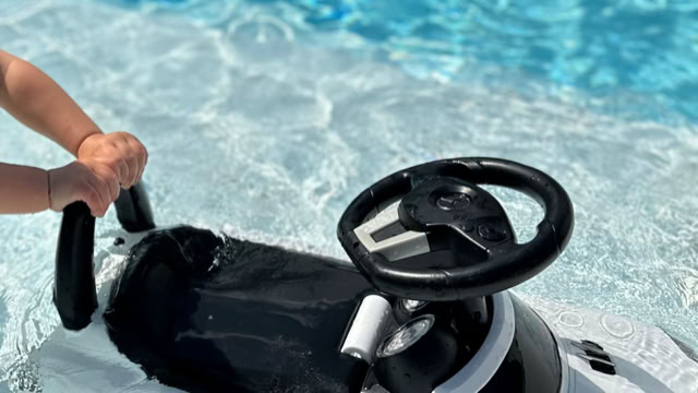 Ein Kind hält ein Lenkradspielzeug im Wasser eines Pools.